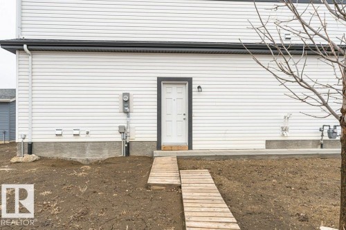 The property features white horizontal siding, a white entry door with dark trim, and a wooden pathway leading to the entrance - 9652 Colak Link Link, Edmonton, AB - Outdoor With Exterior