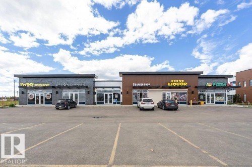 The property features a modern commercial building with multiple storefronts, a prominent parking lot with marked spaces, and a clear view of the sky above - 9652 Colak Link Link, Edmonton, AB - Outdoor