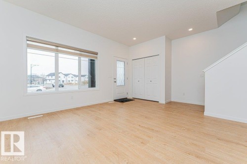 Bright and open living space featuring light-toned hardwood floors, a large window with blinds, and white walls - 9652 Colak Link Link, Edmonton, AB - Indoor Photo Showing Other Room