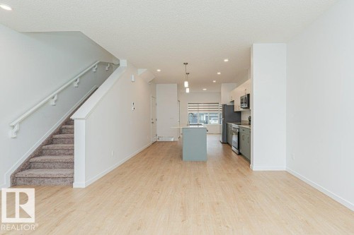 Open concept living space featuring light wood-look flooring, a kitchen island with pendant lighting, and a modern kitchen with grey cabinetry and stainless steel appliances - 9652 Colak Link Link, Edmonton, AB - Indoor Photo Showing Other Room