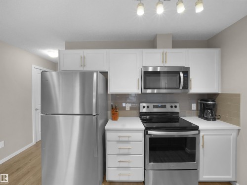 The kitchen features white cabinetry, stainless steel appliances, a tile backsplash, and track lighting - 214 394 Windermere Road, Edmonton, AB - Indoor Photo Showing Kitchen