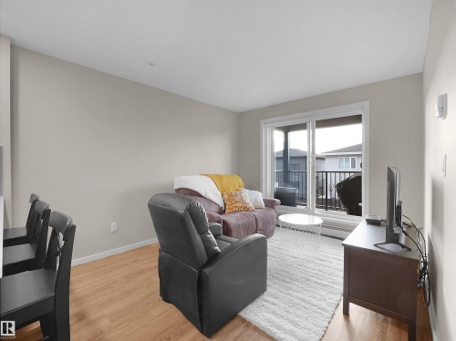 The living area features light wood flooring and a sliding glass door that opens to a balcony - 214 394 Windermere Road, Edmonton, AB - Indoor Photo Showing Living Room