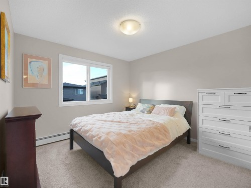 This room features light-colored walls, carpeted flooring, and a window with white trim - 214 394 Windermere Road, Edmonton, AB - Indoor Photo Showing Bedroom