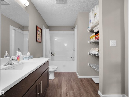 Bathroom featuring a vanity with a white countertop and dark wood cabinetry, a built-in bathtub with a shower, and wire shelving for storage - 214 394 Windermere Road, Edmonton, AB - Indoor Photo Showing Bathroom