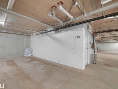 The property features a dedicated storage room with a numbered door, a concrete floor, and exposed overhead piping - 214 394 Windermere Road, Edmonton, AB - Indoor Photo Showing Garage