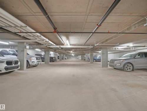 Underground parking garage featuring concrete pillars and ceiling, overhead lighting, and exposed piping - 214 394 Windermere Road, Edmonton, AB - Indoor Photo Showing Garage