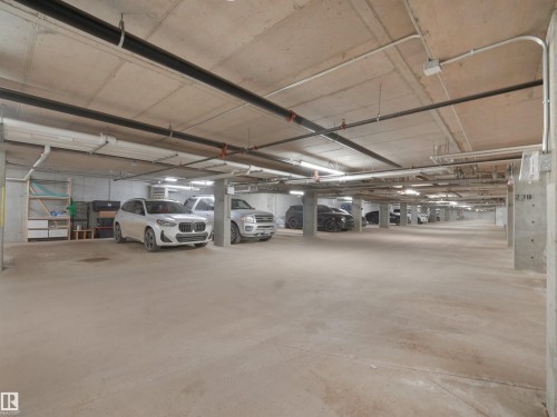 The property includes an underground parking area with concrete floors and ceilings, featuring overhead lighting and visible utility pipes - 214 394 Windermere Road, Edmonton, AB - Indoor Photo Showing Garage
