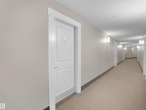 Entryway to the property featuring a white paneled door, light-colored walls, and a textured carpeted hallway - 214 394 Windermere Road, Edmonton, AB - Indoor Photo Showing Other Room