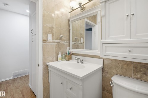 The bathroom features a white vanity with a single basin sink, a wall-mounted mirror, and tile flooring and walls - 16049 95 Avenue, Edmonton, AB - Indoor Photo Showing Bathroom