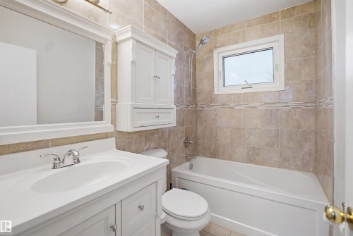 Bathroom featuring a white vanity with an integrated sink, a mirror, and a bathtub with tiled walls - 16049 95 Avenue, Edmonton, AB - Indoor Photo Showing Bathroom