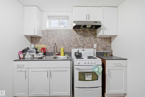 The kitchen features white cabinetry, a double basin sink, and a white oven with a range hood - 16049 95 Avenue, Edmonton, AB - Indoor Photo Showing Kitchen With Double Sink