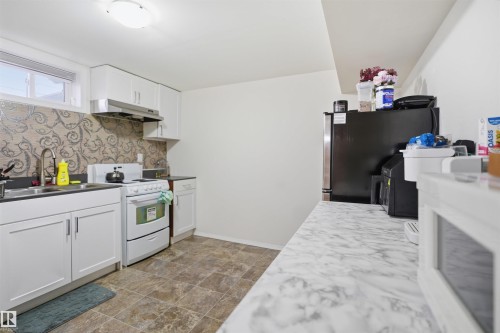 The kitchen features white cabinetry, a stainless steel sink, a modern range hood, and a decorative tile backsplash - 16049 95 Avenue, Edmonton, AB - Indoor