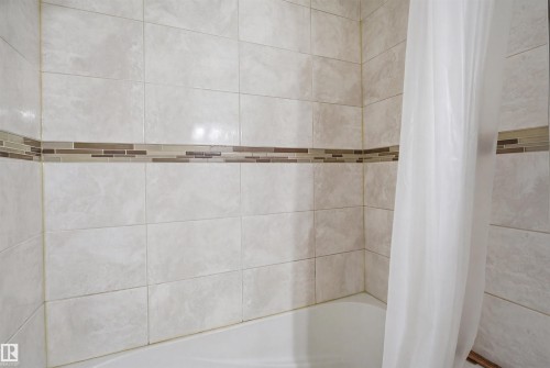 Bathtub and shower surround with light-colored tile and decorative accent band - 16049 95 Avenue, Edmonton, AB - Indoor Photo Showing Bathroom