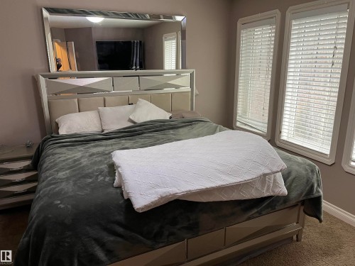 This room features a bed with a reflective headboard and a decorative mirror mounted above it - 21917 95A Avenue, Edmonton, AB - Indoor Photo Showing Bedroom
