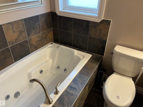 The bathroom features a built-in tub with brushed nickel fixtures and a tiled surround, alongside a white toilet - 21917 95A Avenue, Edmonton, AB - Indoor Photo Showing Bathroom