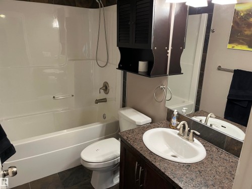 Bathroom featuring a white bathtub and shower combination, a toilet, a vanity with an oval sink, and a dark wood cabinet - 21917 95A Avenue, Edmonton, AB - Indoor Photo Showing Bathroom