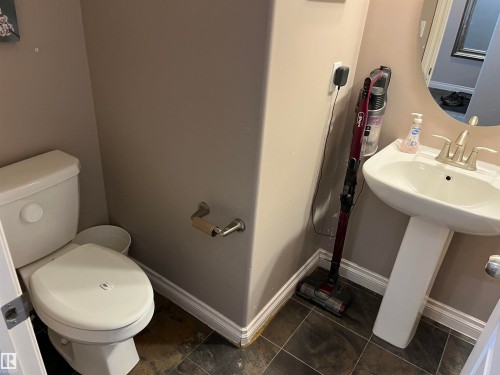 Bathroom featuring a white toilet, a white pedestal sink with a brushed nickel faucet, and dark tile flooring - 21917 95A Avenue, Edmonton, AB - Indoor Photo Showing Bathroom
