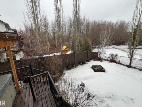 The property includes a spacious backyard with a wooden fence, a fire pit, and a path leading into a wooded area - 21917 95A Avenue, Edmonton, AB - Outdoor