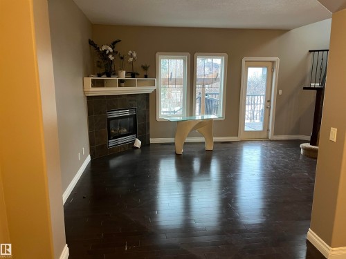 Spacious living area featuring dark hardwood flooring, a tiled fireplace with a white mantel, and windows that provide natural light and views of the outdoors - 21917 95A Avenue, Edmonton, AB - Indoor Photo Showing Living Room With Fireplace