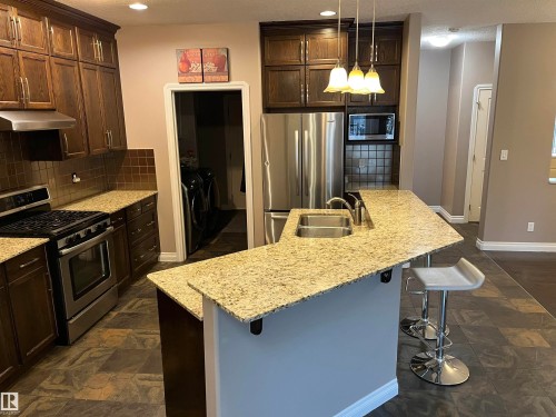 The kitchen features dark wood cabinetry, granite countertops, and stainless steel appliances including a gas range and refrigerator - 21917 95A Avenue, Edmonton, AB - Indoor Photo Showing Kitchen With Double Sink