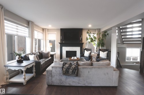 This inviting living space features dark wood flooring, a fireplace with a white tile surround and dark mantel, and recessed lighting - 1003 Huckell Place, Edmonton, AB - Indoor Photo Showing Living Room With Fireplace