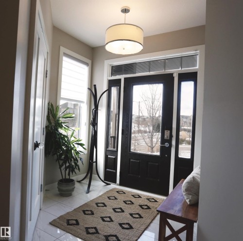 Welcoming entryway featuring a dark-paneled front door with glass inserts, white tile flooring, and a modern drum pendant light fixture - 1003 Huckell Place, Edmonton, AB - Indoor Photo Showing Other Room