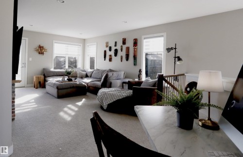 Bright living area featuring light-colored carpeting, large windows, and a brick-faced column - 1003 Huckell Place, Edmonton, AB - Indoor Photo Showing Living Room