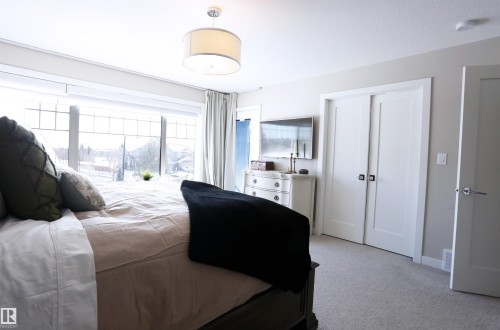 Bedroom featuring light-colored carpet flooring, a large window with multiple panes, and a modern drum pendant light fixture - 1003 Huckell Place, Edmonton, AB - Indoor Photo Showing Bedroom