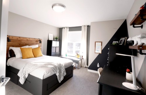 This bedroom features a stylish wooden headboard, a window with natural light, and a contrasting accent wall with geometric design - 1003 Huckell Place, Edmonton, AB - Indoor Photo Showing Bedroom