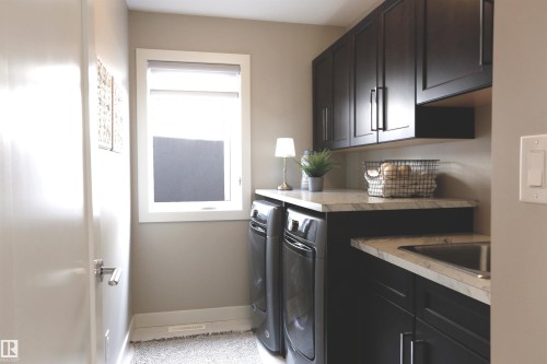 Laundry room featuring dark cabinetry with light countertops, a sink, and a window - 1003 Huckell Place, Edmonton, AB - Indoor Photo Showing Laundry Room