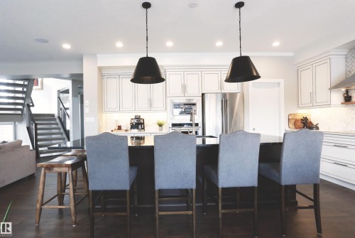 This kitchen features white cabinetry, a stainless steel refrigerator, and pendant lighting - 1003 Huckell Place, Edmonton, AB - Indoor