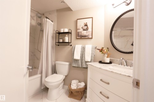 Bathroom featuring a white vanity with a marble countertop, a round mirror with a textured frame, and a bathtub with a shower - 1003 Huckell Place, Edmonton, AB - Indoor Photo Showing Bathroom