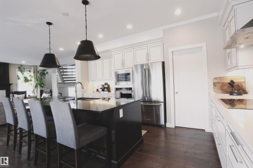 The kitchen features dark wood flooring, a central island with seating, a stainless steel refrigerator, and white cabinetry - 1003 Huckell Place, Edmonton, AB - Indoor Photo Showing Kitchen With Upgraded Kitchen