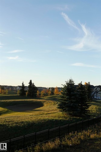 The property features views of a landscaped green space with mature trees and a sand trap, bordered by a dark metal fence - 1003 Huckell Place, Edmonton, AB - Outdoor With View