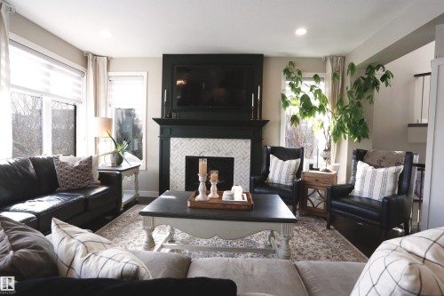 Living area featuring a fireplace with a herringbone tile surround and a dark mantel, large windows with blinds, and recessed lighting - 1003 Huckell Place, Edmonton, AB - Indoor Photo Showing Living Room With Fireplace