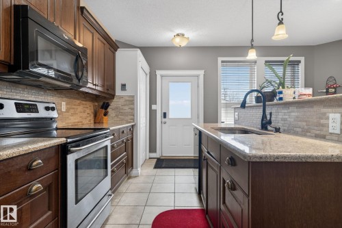 The kitchen features dark wood cabinetry, granite countertops, stainless steel appliances, and a tiled backsplash - 10418 69 Avenue, Edmonton, AB - Indoor Photo Showing Kitchen With Upgraded Kitchen