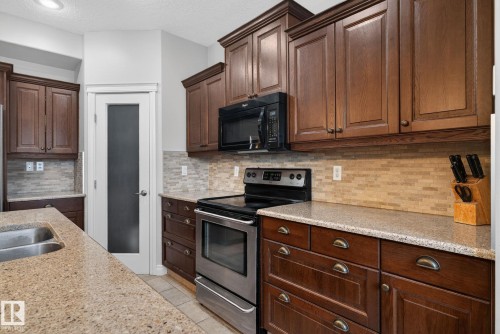 The kitchen features rich wood cabinetry, granite countertops, and a full suite of stainless steel appliances, including an oven and microwave - 10418 69 Avenue, Edmonton, AB - Indoor Photo Showing Kitchen With Double Sink