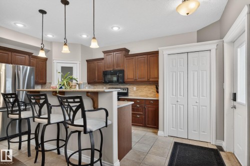 The kitchen features wood cabinetry, stainless steel appliances, and a breakfast bar with pendant lighting - 10418 69 Avenue, Edmonton, AB - Indoor Photo Showing Kitchen With Stainless Steel Kitchen With Upgraded Kitchen