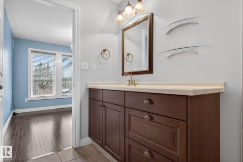 Bathroom vanity with a light-colored countertop, dark wood cabinetry, and a framed mirror - 10418 69 Avenue, Edmonton, AB - Indoor Photo Showing Bathroom