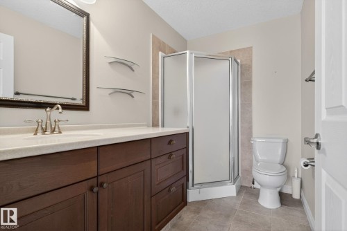 Well-appointed bathroom featuring a dark wood vanity with a light-colored countertop, a framed mirror, a corner shower with a glass enclosure, and tiled flooring - 10418 69 Avenue, Edmonton, AB - Indoor Photo Showing Bathroom