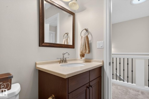 This bathroom features a vanity with a light-colored countertop and a dark wood cabinet, a framed mirror, and a wall-mounted light fixture - 10418 69 Avenue, Edmonton, AB - Indoor Photo Showing Bathroom