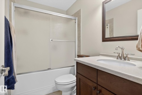 Bathroom featuring a dark wood vanity with a light-colored countertop, a white toilet, and a bathtub with a frosted sliding glass enclosure - 10418 69 Avenue, Edmonton, AB - Indoor Photo Showing Bathroom