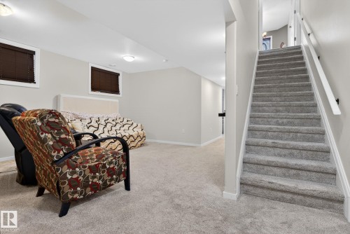 This versatile room features light-colored carpeting, two windows with brown blinds, and a staircase with a white handrail leading to an upper level - 10418 69 Avenue, Edmonton, AB - Indoor Photo Showing Other Room