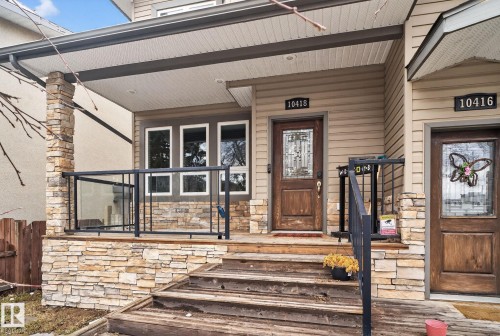 The property features a stone-clad porch with glass panel railings, a solid wood entry door with decorative glass, and horizontal siding - 10418 69 Avenue, Edmonton, AB - Outdoor