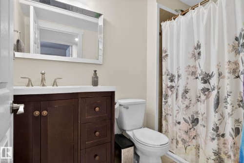 Bathroom featuring a vanity with a white countertop and dark wood cabinetry, a toilet, and a shower with a patterned curtain - 10418 69 Avenue, Edmonton, AB - Indoor Photo Showing Bathroom