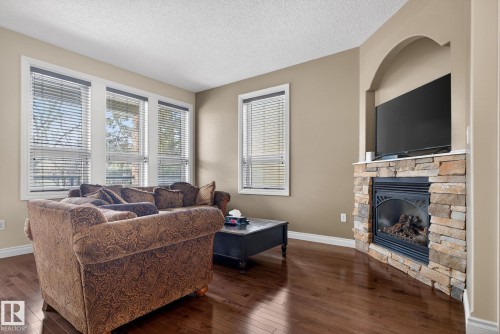 The living room features rich hardwood floors, a stone fireplace with a mantel, and an arched niche above the fireplace - 10418 69 Avenue, Edmonton, AB - Indoor Photo Showing Living Room With Fireplace