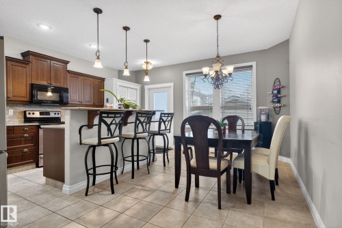 Open concept kitchen and dining area with tile flooring, a kitchen island with pendant lighting, dark wood cabinetry, and a window providing natural light - 10418 69 Avenue, Edmonton, AB - Indoor