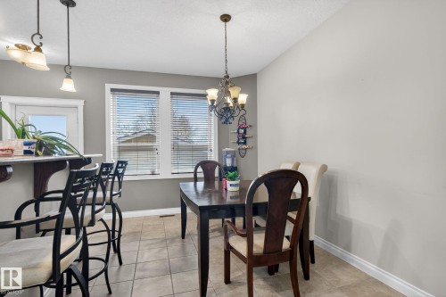 The dining area features tiled flooring, a chandelier, and a window with blinds - 10418 69 Avenue, Edmonton, AB - Indoor Photo Showing Dining Room