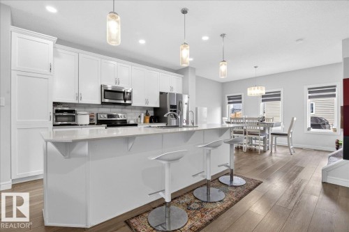 The kitchen features white cabinetry, stainless steel appliances, and a central island with a light-colored countertop - 203 Cavanagh Common, Edmonton, AB - Indoor Photo Showing Kitchen With Upgraded Kitchen