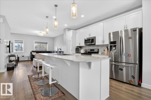 This open-concept living space features light wood flooring, recessed lighting, and large windows - 203 Cavanagh Common, Edmonton, AB - Indoor Photo Showing Kitchen With Upgraded Kitchen